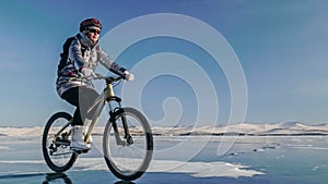 Woman is riding bicycle on the ice. Tires on bike are covered wi