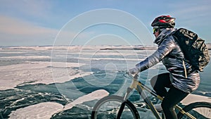 Woman is riding bicycle on the ice. Tires on bike are covered wi