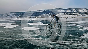 Woman is riding bicycle on the ice. Tires on bike are covered wi