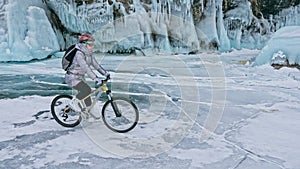 Woman is riding bicycle near the ice grotto. The rock with ice c