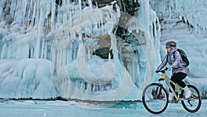 Woman is riding bicycle near the ice grotto. The rock with ice c