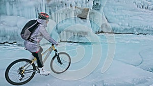 Woman is riding bicycle near the ice grotto. The rock with ice c