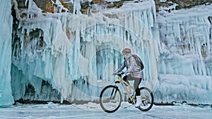 Woman is riding bicycle near the ice grotto. The rock with ice c