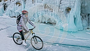 Woman is riding bicycle near the ice grotto. The rock with ice c