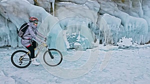 Woman is riding bicycle near the ice grotto. The rock with ice c