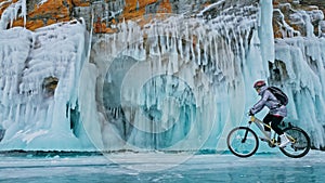 Woman is riding bicycle near the ice grotto. The rock with ice c