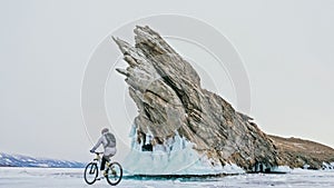 Woman is riding bicycle near the ice grotto. The rock with ice c