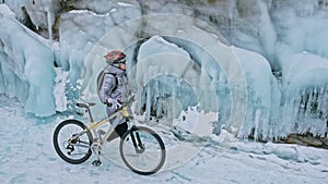 Woman is riding bicycle near the ice grotto. The rock with ice c