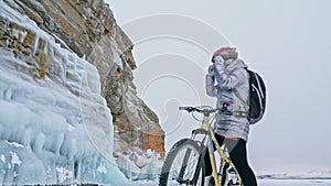 Woman is riding bicycle near the ice grotto. The rock with ice c