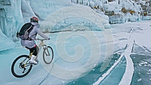 Woman is riding bicycle near the ice grotto. The rock with ice c