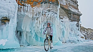 Woman is riding bicycle near the ice grotto. The rock with ice c