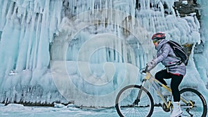 Woman is riding bicycle near the ice grotto. The rock with ice c