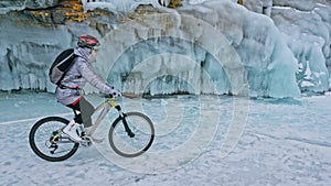 Woman is riding bicycle near the ice grotto. The rock with ice c