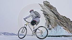 Woman is riding bicycle near the ice grotto. The rock with ice caves and icicles is very beautiful. The girl is dressed