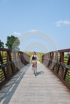 Woman riding bicycle over bridge on bike path