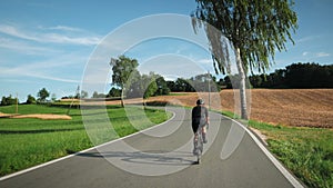 Woman riding bicycle through yellow wheat field and green meadow. Professional female cyclist in cycling apparel pushing pedals on