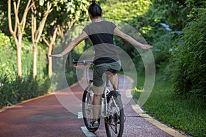 Woman riding a bike on sunny park trail with arms