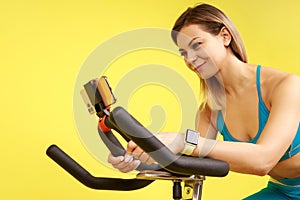 Woman riding exercise bike and using her mobile phone for broadcasting her cardio workout online.