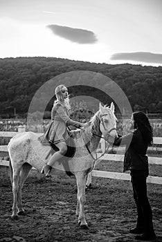 Woman riding grey arabian horse in pink dress. Handsome bearded man driving horse for a bridle and looking at his