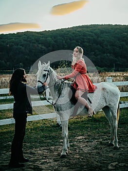 Woman riding grey arabian horse in pink dress. Handsome bearded man driving horse for a bridle and looking at his