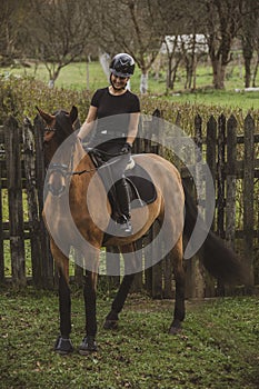 Woman riding her brown horse with black mane dressed in black with a helmet