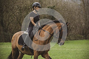 Woman riding her brown horse with black mane dressed in black with a helmet