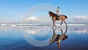 Woman riding horse on beach along sea by water pool