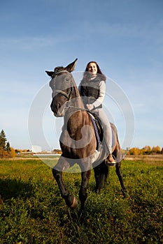 Woman riding a horse in filed in autumn day and blue sky background