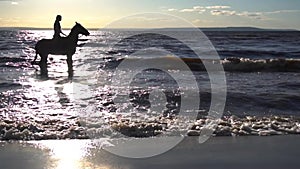 Woman riding on horse at river beach in water sunset light