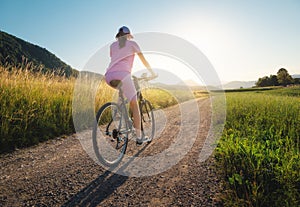Woman is riding a mountain bike on gravel road at sunset