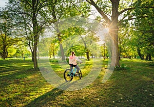 Woman riding a mountain bike near green trees at sunset in sprin