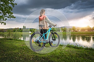 Woman riding a mountain bike near lake and overcast sky in sprin