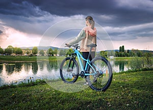 Woman riding a mountain bike near lake and overcast sky in sprin