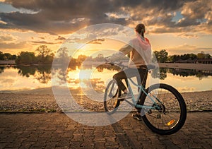 Woman riding a mountain bike near lake at sunset in summer