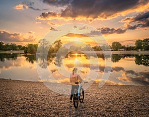 Woman riding a mountain bike near lake at sunset in summer