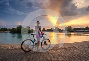 Woman riding a mountain bike near lake at sunset in summer