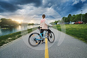 Woman riding a mountain bike on the road near lake at sunset