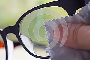 Woman right hand cleaning grey shortsighted or nearsighted eyeglasses by grey microfibre cleaning cloths, Bokeh green bg.