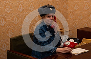 Woman rings from a Russian retro red telephone with a hat on her head