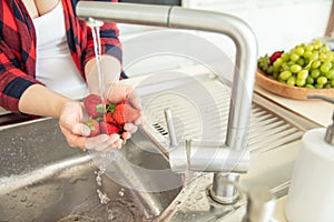 Woman rinses the strawberries in the kitchen photo