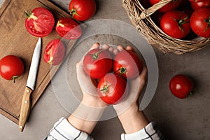 Woman with ripe tomatoes at grey table, top view