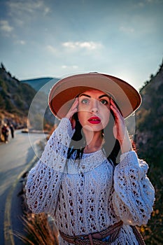 Woman road mountain. A woman in a white sweater, black boots and a hat walks along a winding alpine path between the
