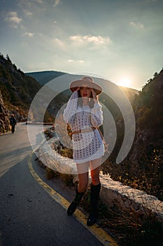 Woman road mountain. A woman in a white sweater, black boots and a hat walks along a winding alpine path between the