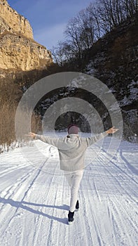 Woman on the road in winter. Young woman walks alone on a winter road among steep rocks, keeping balance.