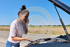 Woman on the roadside near broken car talking on cell phone