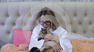A woman in a robe is lying in bed with a cat in her hands and stroking the cat