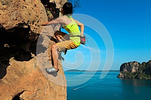 Woman rock climber climbing at seaside cliff