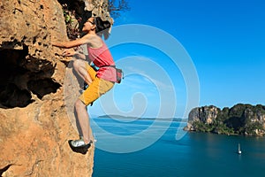 Woman rock climber climbing at seaside cliff