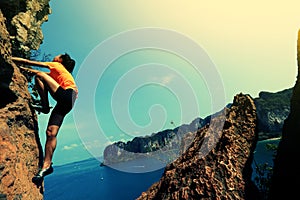Woman rock climber climbing on seaside mountain cliff