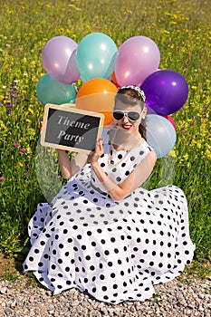 Woman with a rock n Roll dress and balloons holding a slate with text theme party